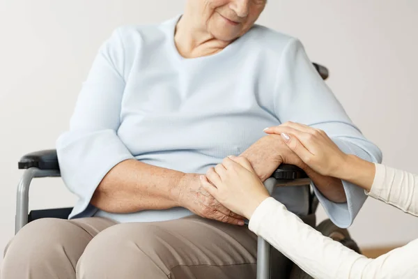 elderly woman in a wheelchair is holding the hands of a family member