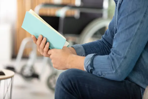 Young man on wheelchair reading a book at home