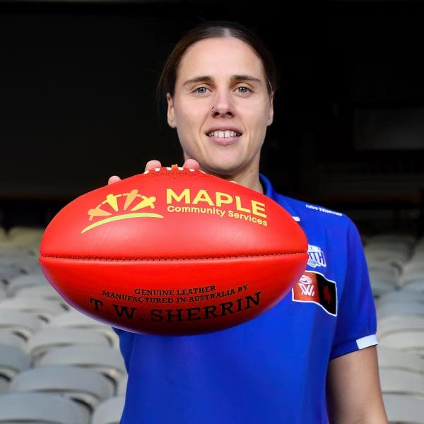 AFLW players holding a Maple Community Services branded football in the stadium stands